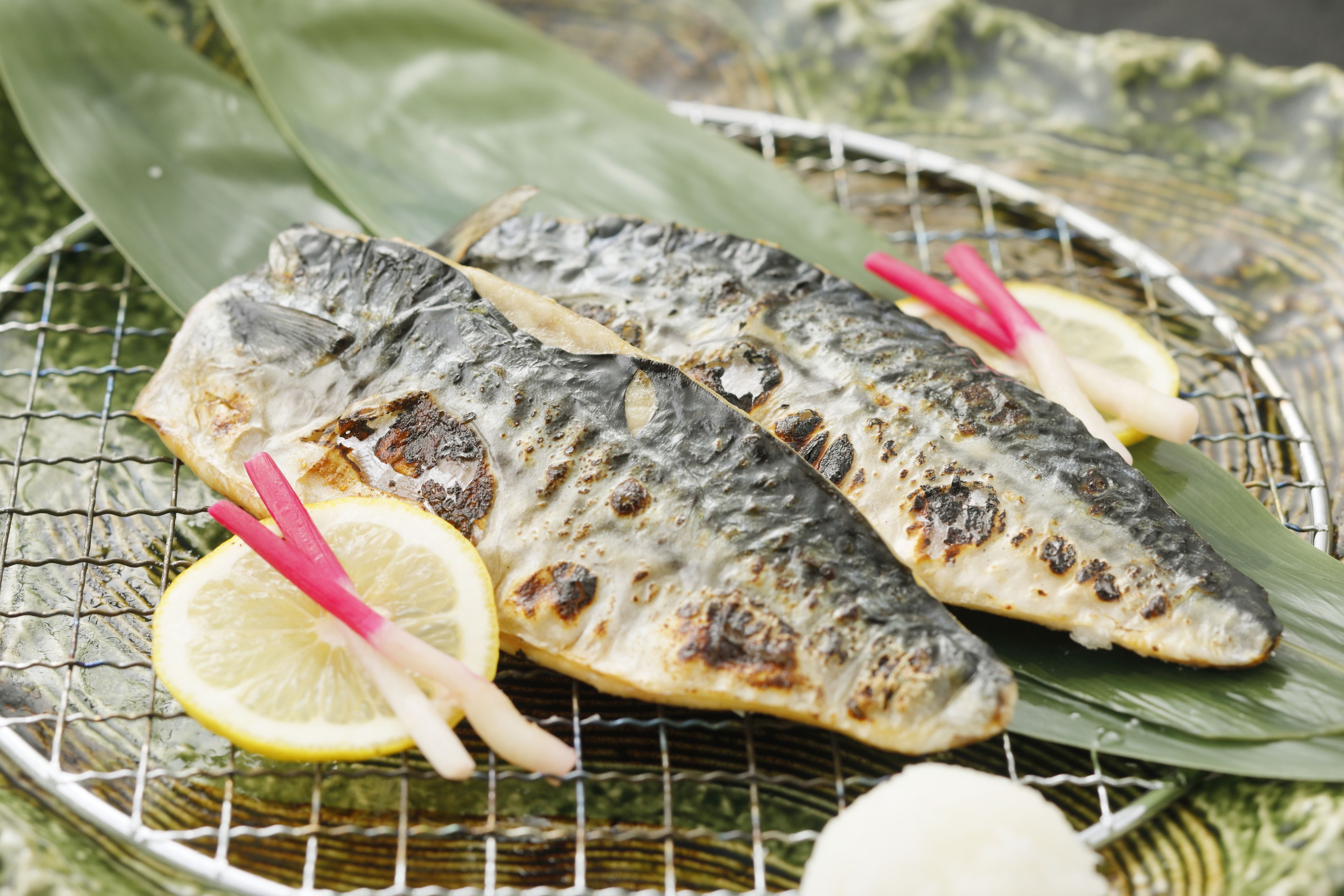 Grilled fish on a wire rack with lemon slices and herbs.