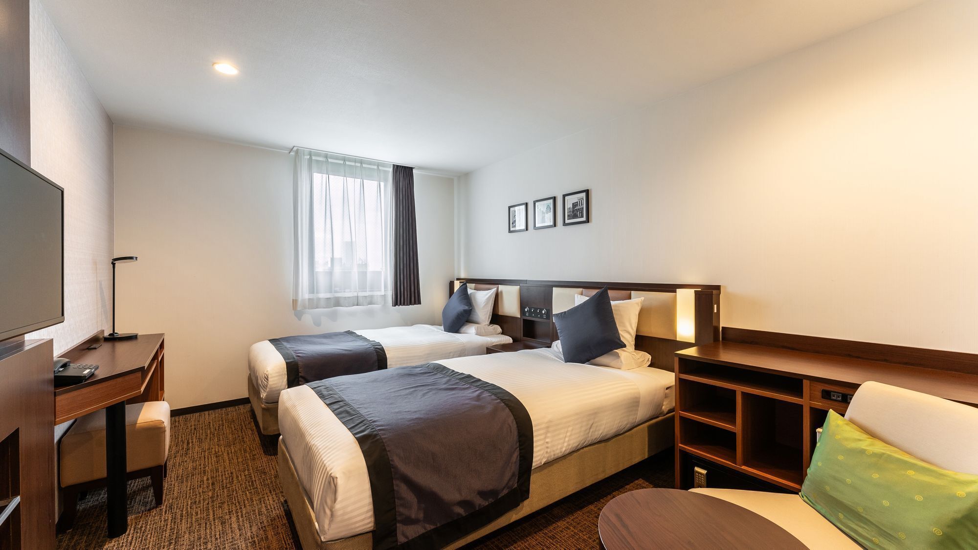 A hotel room with two beds, a desk, a chair, a TV, and a window with curtains.