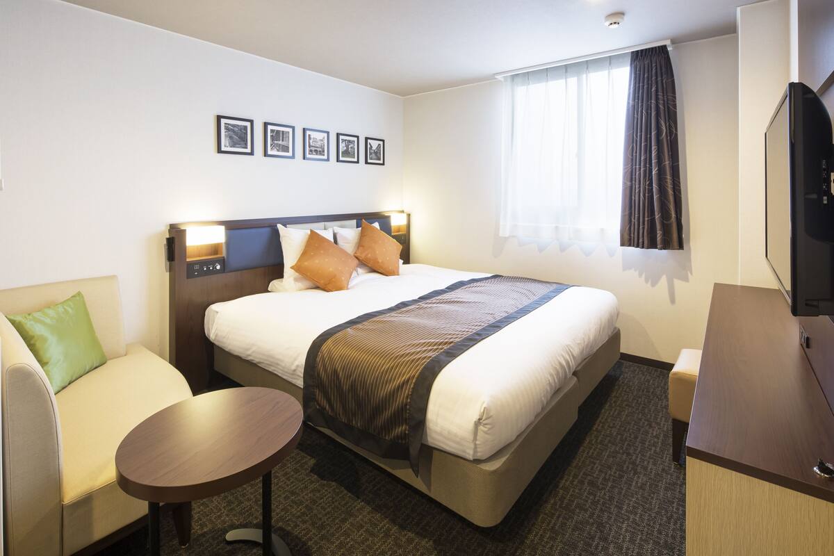 Ein Hotelzimmer mit einem Bett, einer Sitzecke, einem kleinen Tisch, einem Fernseher und gerahmten Bildern an der Wand.
