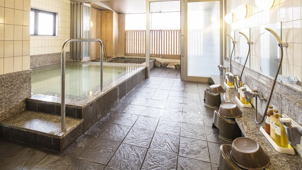 Un onsen japonés tradicional con un baño de piedra, escalones de madera y suelo de baldosas.