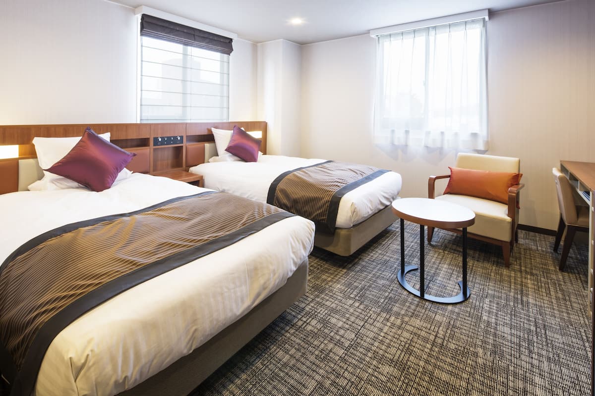 Ein Hotelzimmer mit zwei Betten, einem kleinen runden Tisch und einem Stuhl.