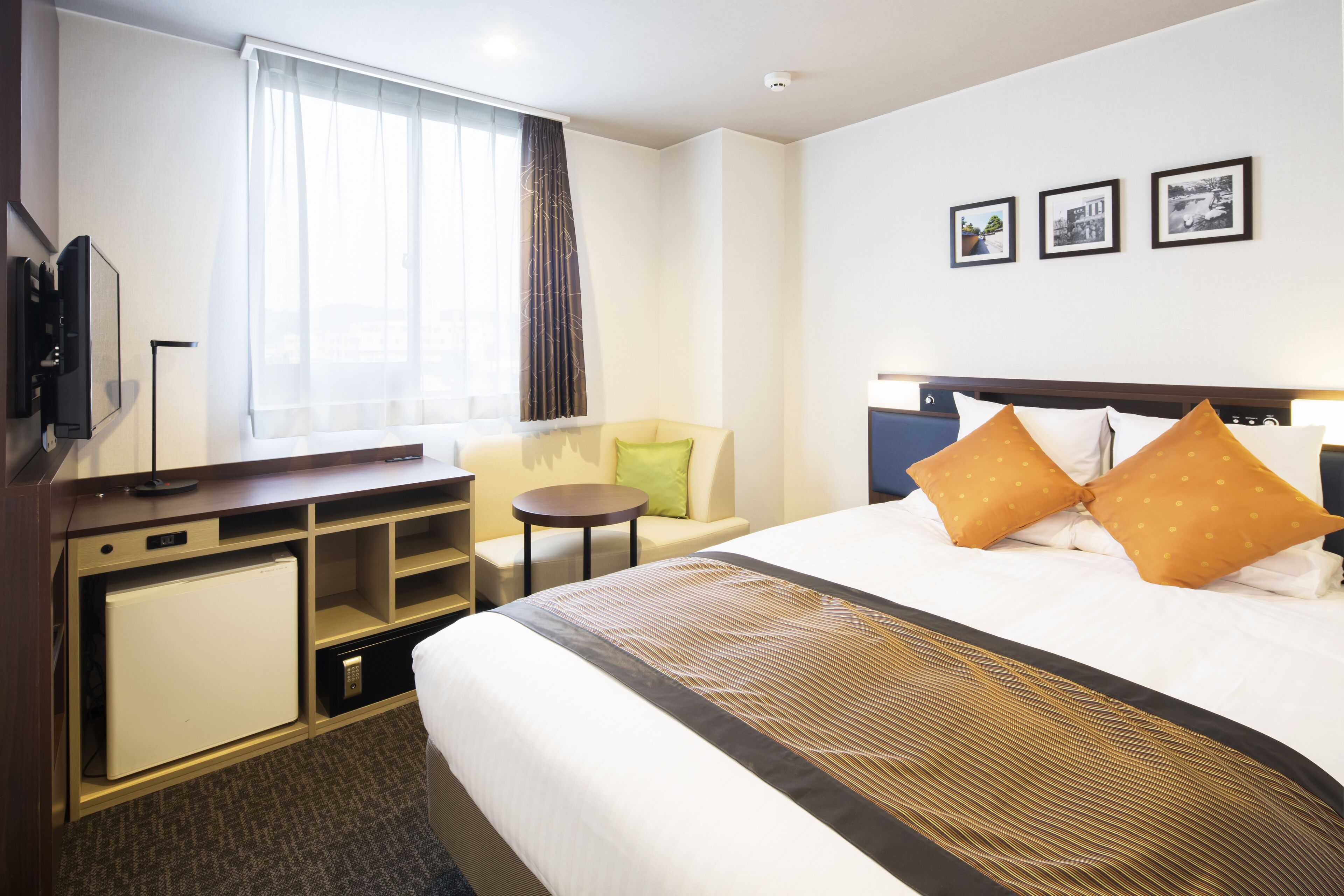 Une chambre d’hôtel avec un lit, un bureau avec un ordinateur, une petite table, une chaise, une télévision et une fenêtre avec des rideaux.