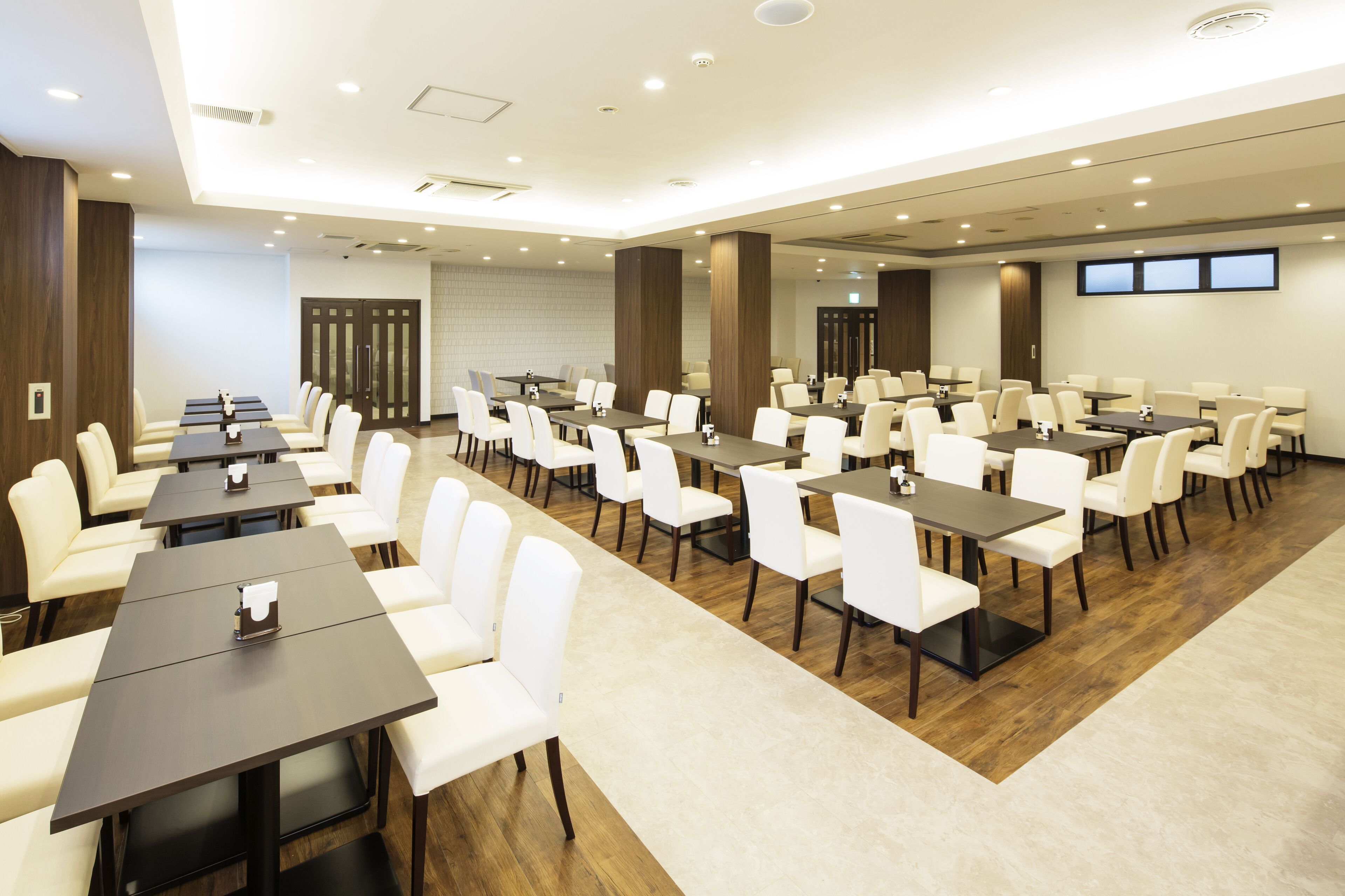 A conference room with multiple tables and chairs, wooden flooring, and a modern ceiling design.