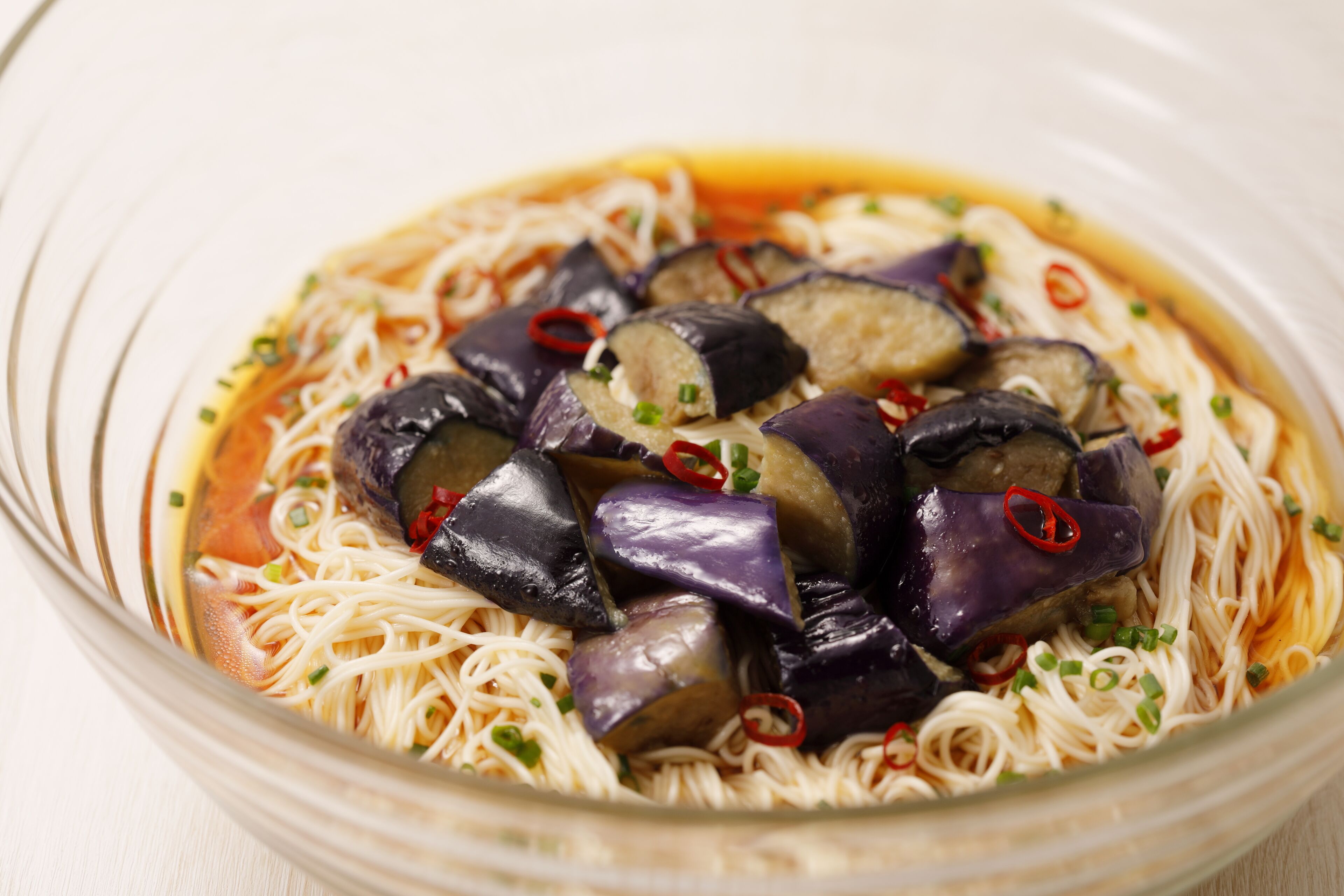 A bowl of noodles with eggplant slices and green onions.