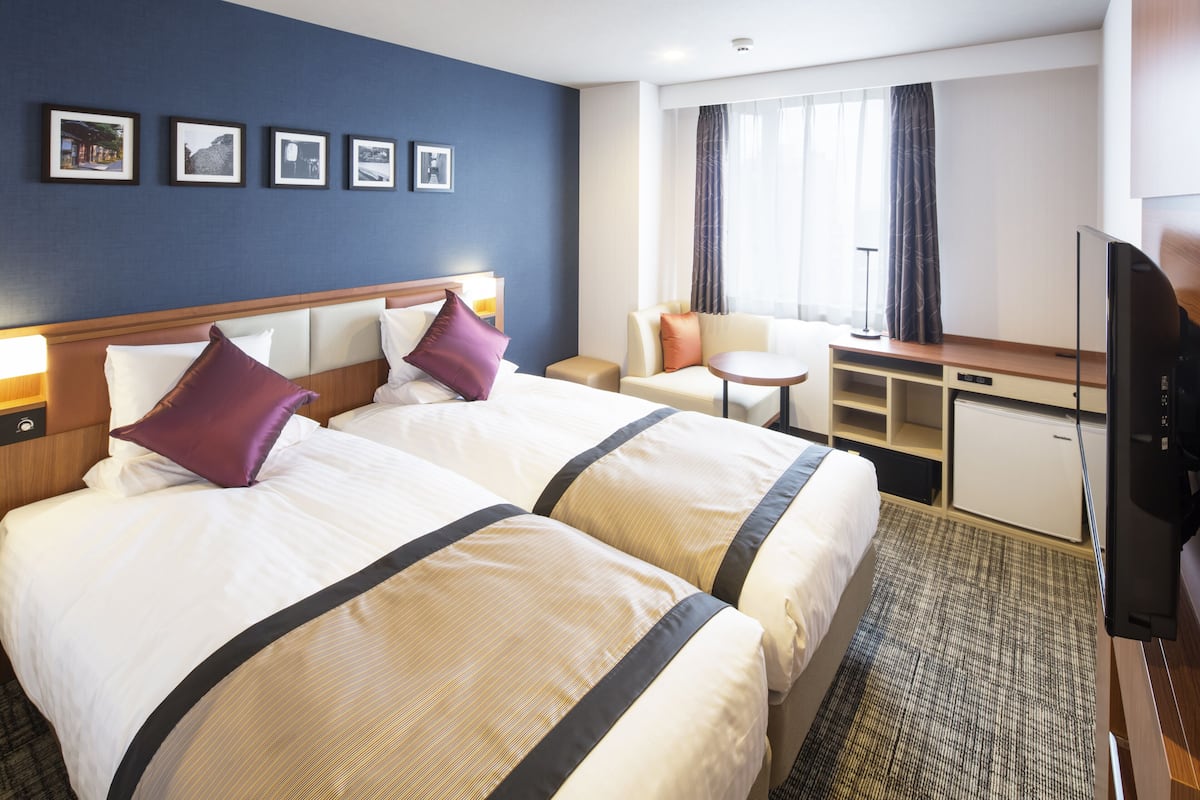 Ein Hotelzimmer mit zwei Betten, einem Schreibtisch, einem Stuhl und einem Fernseher.