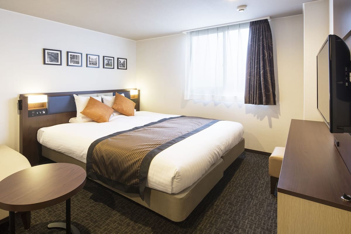 Ein Hotelzimmer mit Bett, kleinem Tisch, Sofa, Fernseher und gerahmten Bildern an der Wand.