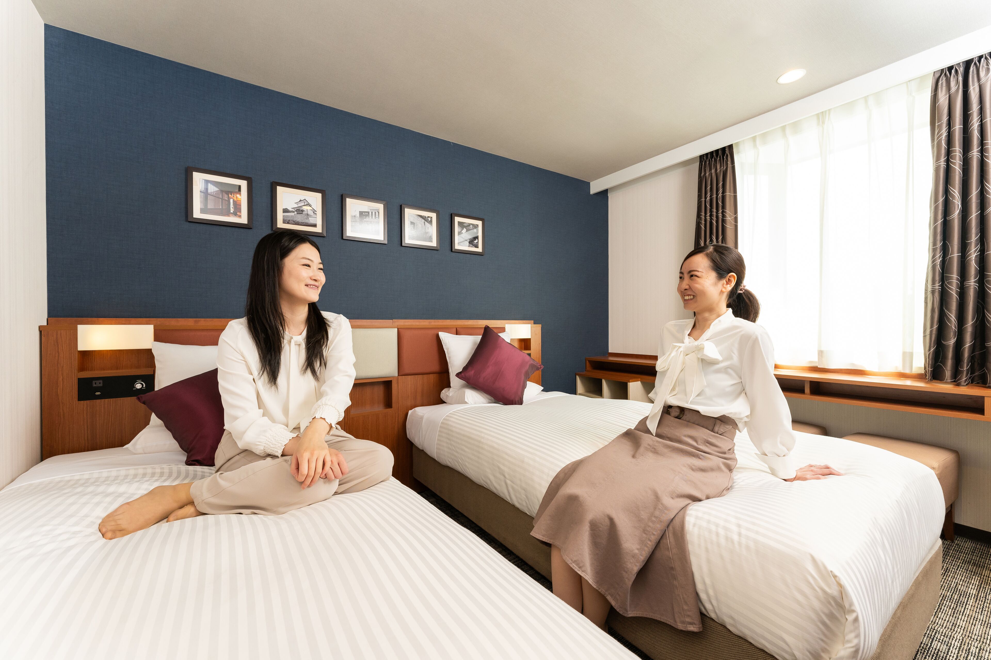 Ein Hotelzimmer mit zwei Betten, einem Holzkopfstück und einem Fenster mit Vorhängen.