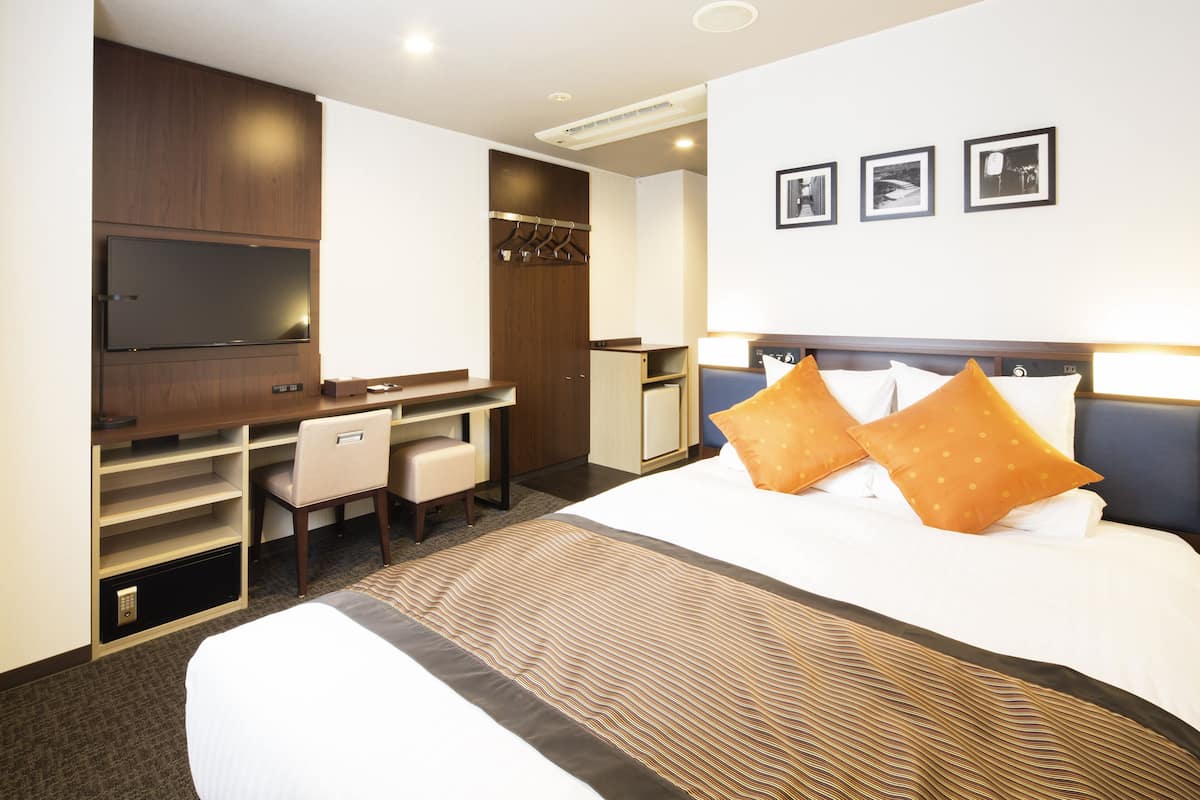 Ein Hotelzimmer mit Bett, Schreibtisch, Stuhl, Fernseher und Kleiderschrank.