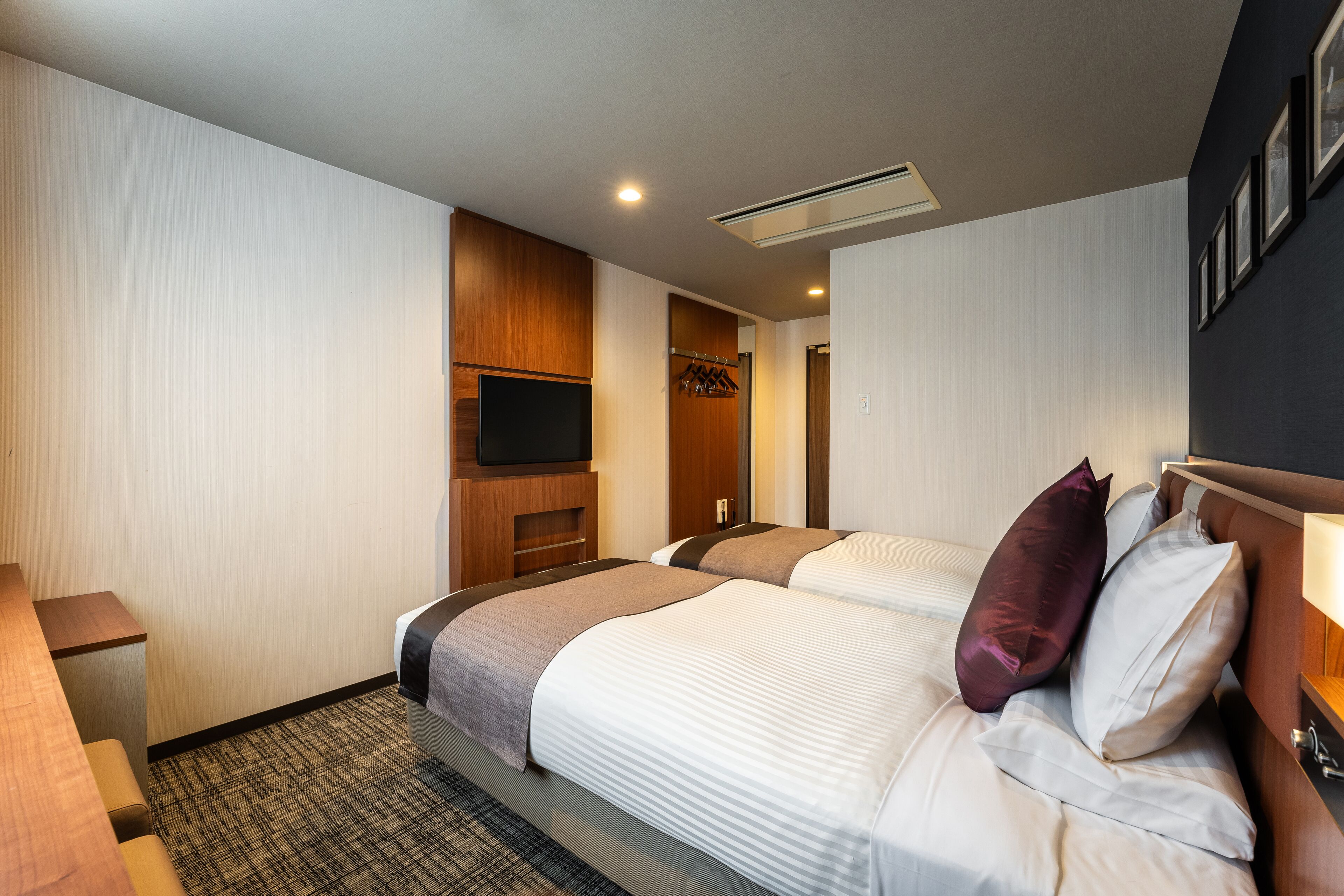 Habitación de hotel con dos camas, un televisor, un mueble de madera y un perchero.