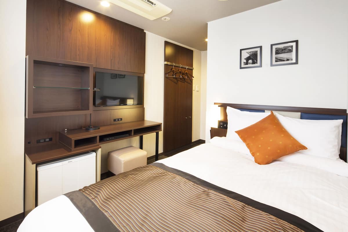 Ein Hotelzimmer mit einem Bett, einem Schreibtisch mit Computer, einem Fernseher und einem Kleiderschrank.