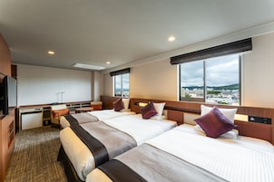 A hotel room with three beds, a desk, and a view of the city.