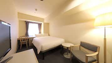 Quarto de hotel com cama, escrivaninha com cadeira, televisão, luminária e janela com cortinas.