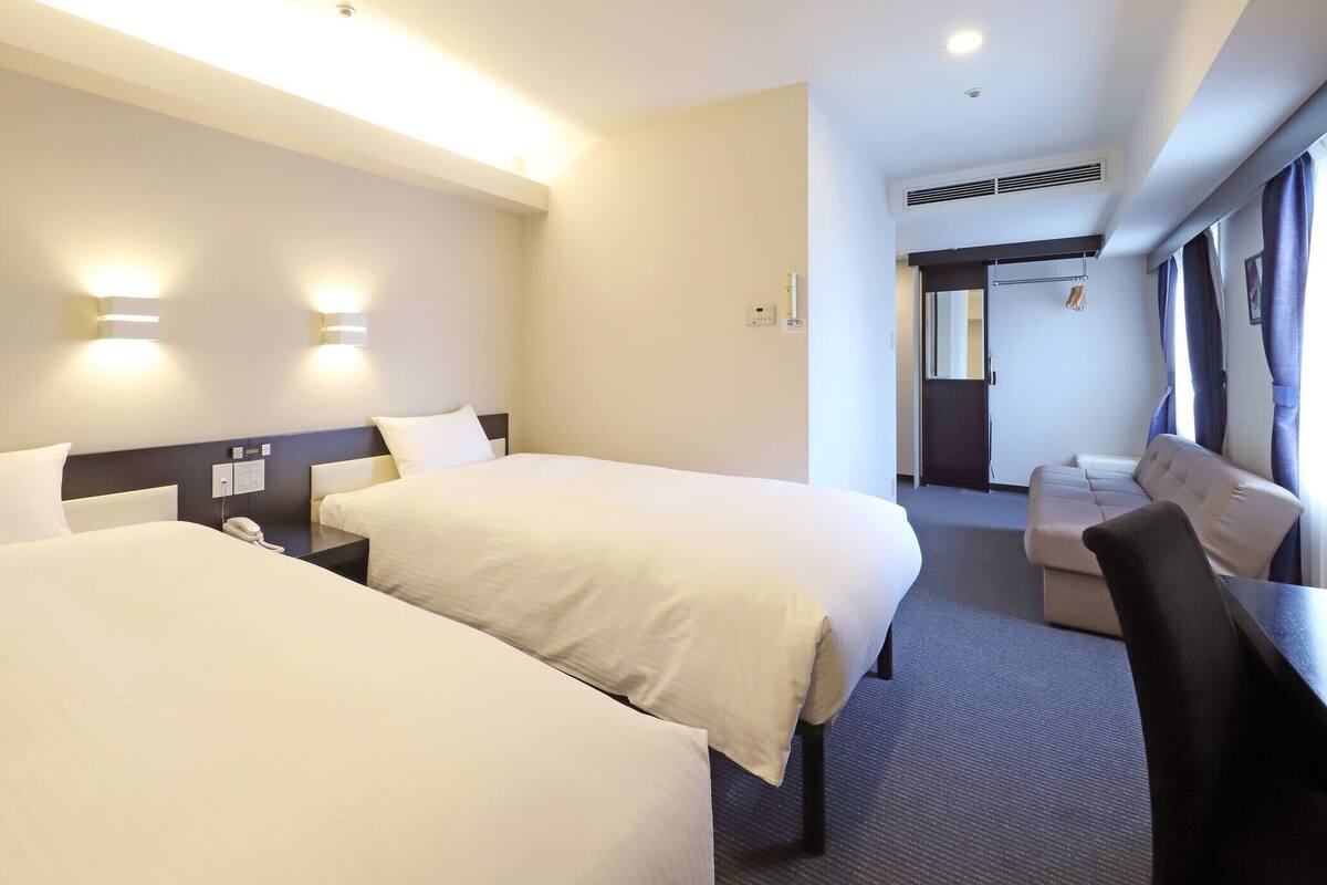 A hotel room with two beds, a desk, and a seating area.