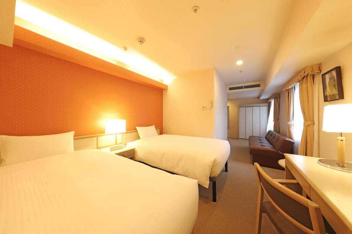 A hotel room with two beds, a desk, a chair, and a sofa.