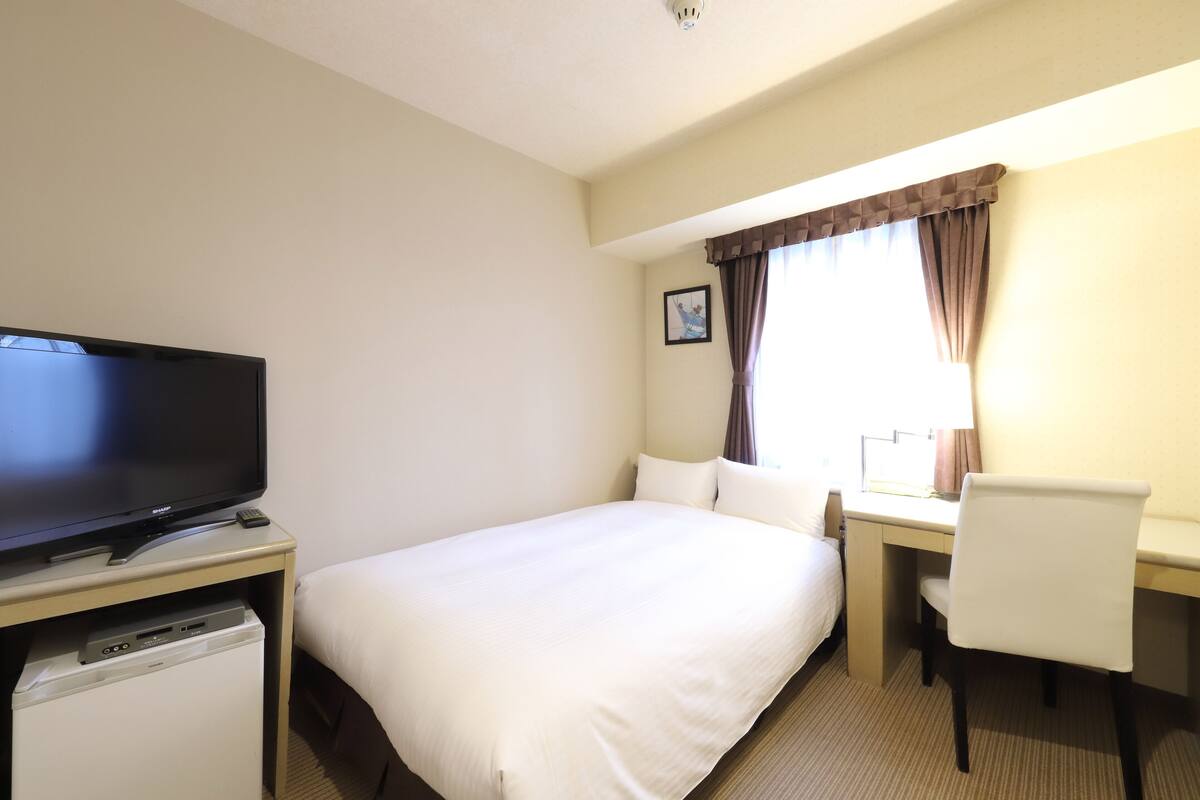 A hotel room with a bed, a desk, a chair, a television, and a small refrigerator.