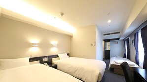 A hotel room with two beds, a desk, and a chair. There are wall-mounted lights and a window with curtains.