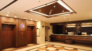 A hotel lobby with a reception desk, elevators, and a patterned floor.
