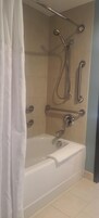 A modern bathroom with a bathtub, grab bars, and a showerhead.