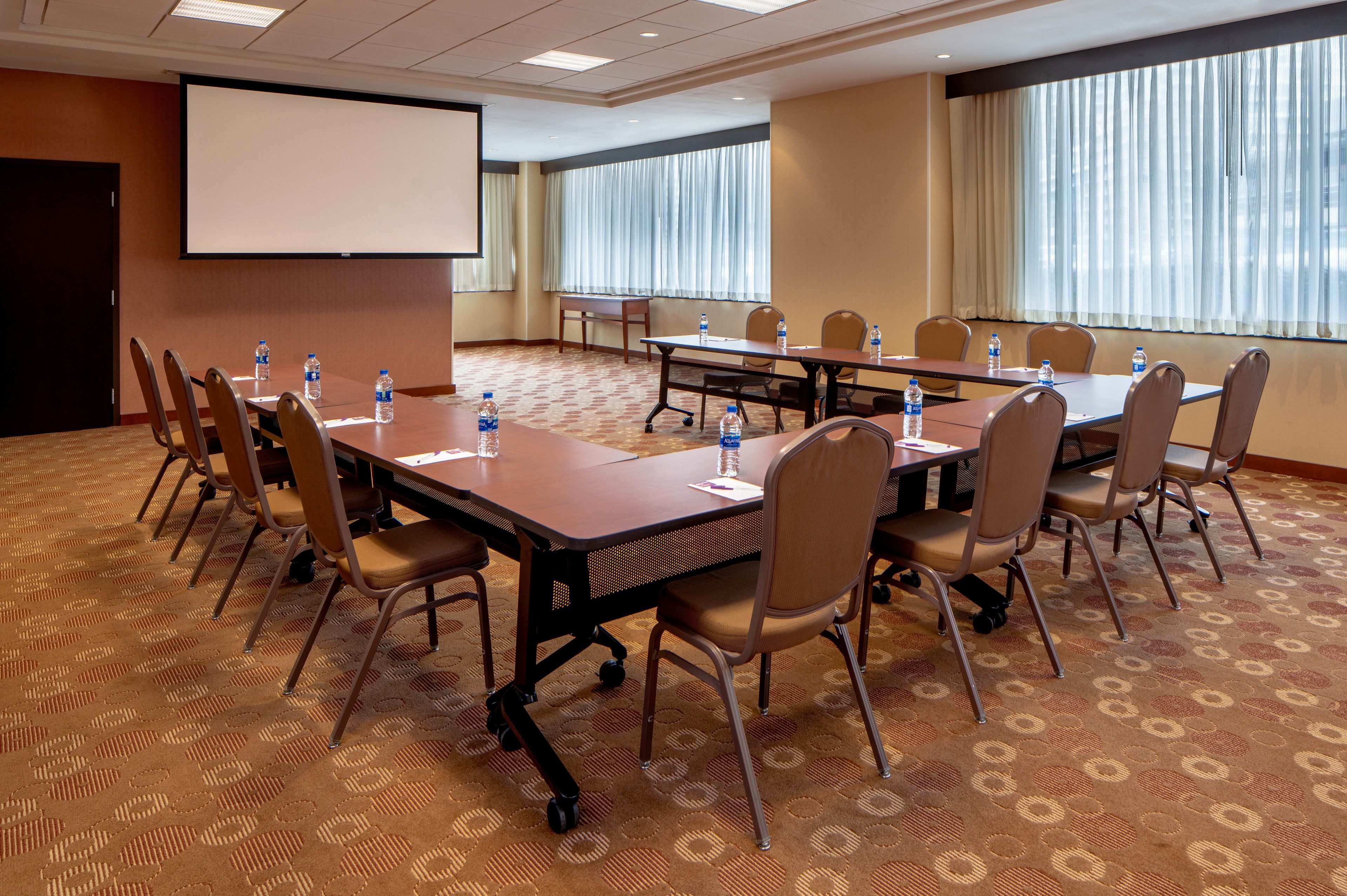 A conference room with a large table, chairs, a projector screen, and water bottles.