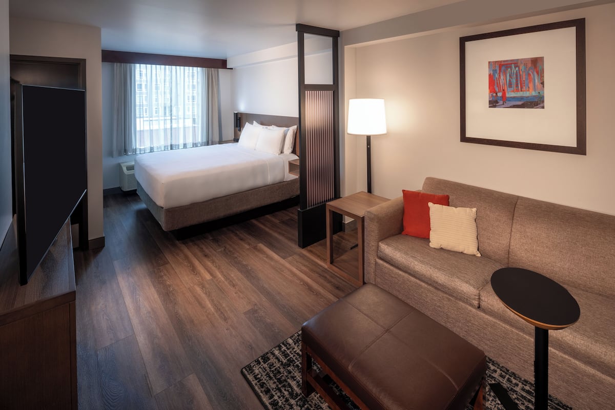 A hotel room with a bed, a sofa, a small table, a lamp, and a framed picture on the wall.