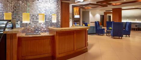 A hotel lobby with a reception desk, blue chairs, and a tiled floor.