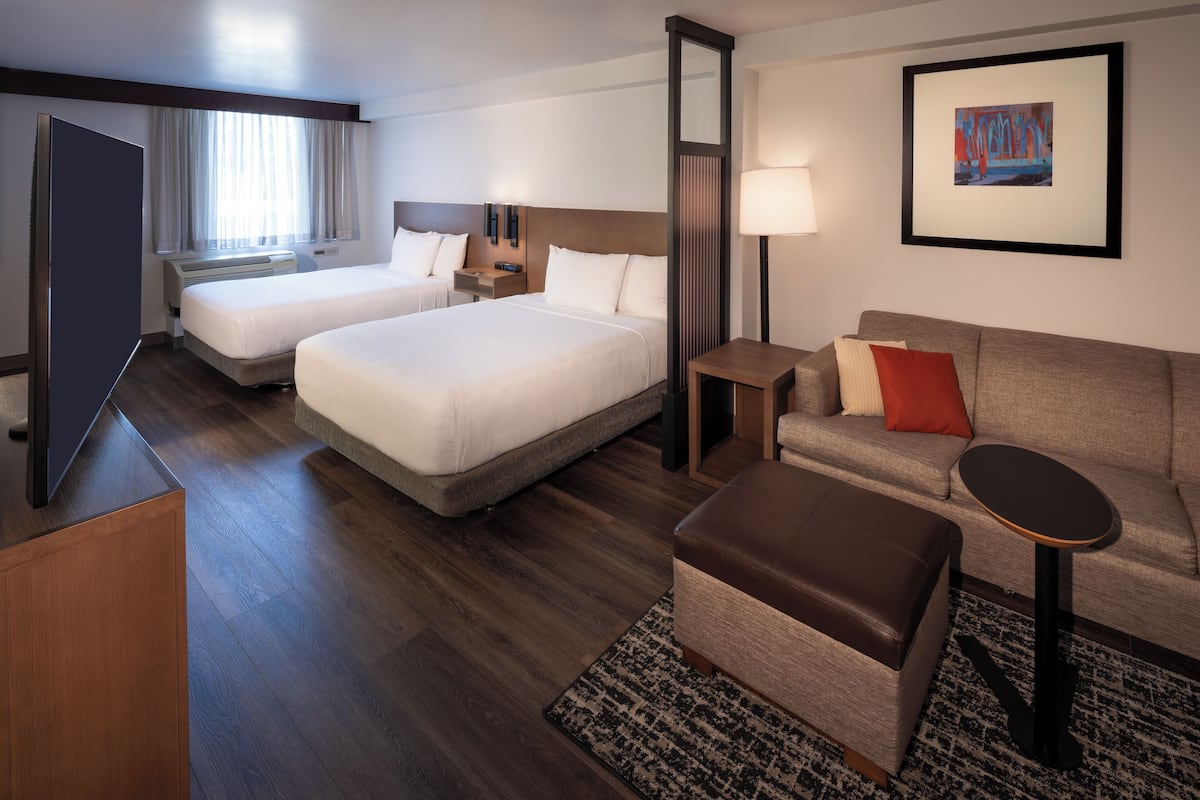 A hotel room with two beds, a sofa, a small table, a TV, and a painting on the wall.