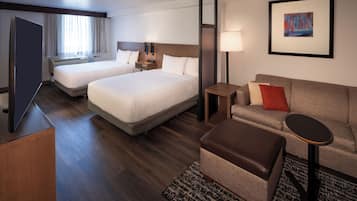 A hotel room with two beds, a sofa, a small table, a TV, and a painting on the wall.
