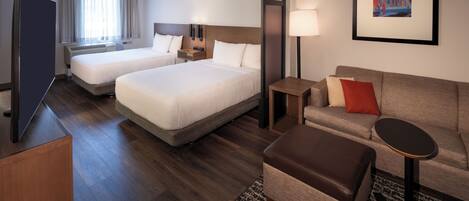 A hotel room with two beds, a sofa, a small table, a TV, and a painting on the wall.
