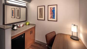 A compact hotel room with a kitchenette, a dining area, and artwork on the walls.