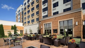 An outdoor patio area with wicker furniture, large windows, and a brick building in the background. - DoubleTree by Hilton Sterling - Dulles Airport (Sterling)