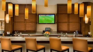 A bar area with wooden cabinets, a flat-screen TV displaying a sports game, and pendant lighting. - DoubleTree by Hilton Sterling - Dulles Airport (Sterling)