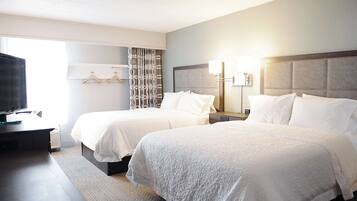 A hotel room with two beds, a desk, a TV, and a window with curtains.