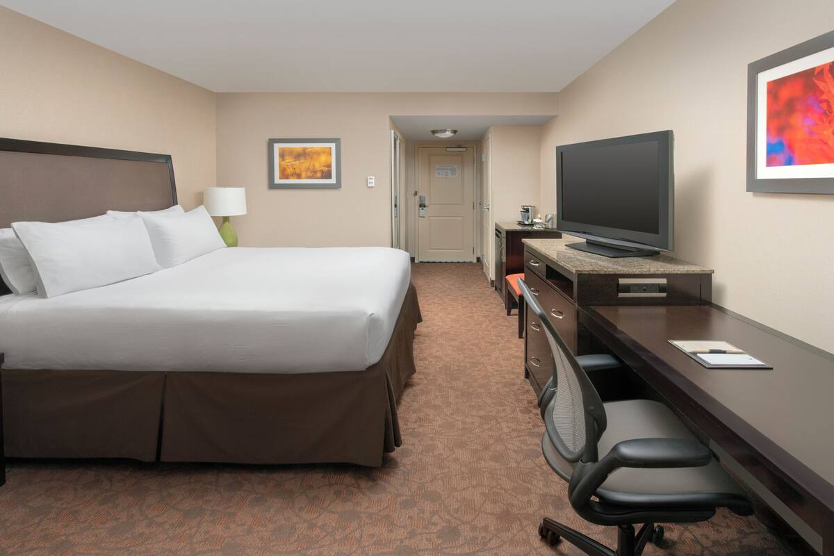 Une chambre d’hôtel avec un grand lit, un bureau avec un ordinateur, une télévision et une chaise.