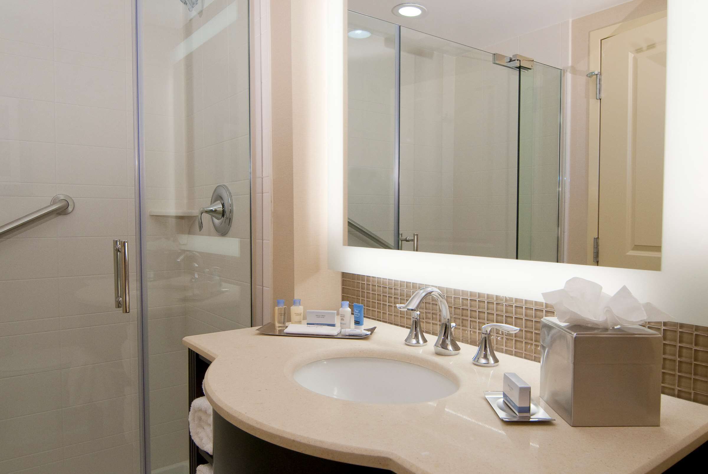 A modern bathroom with a glass shower enclosure, a sink with a mirror above, and toiletries on the counter.
