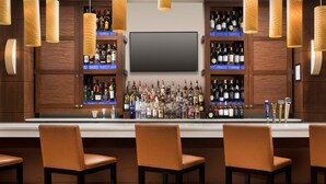A bar area with wooden cabinets, a flat-screen TV, and multiple liquor bottles. - DoubleTree by Hilton Sterling - Dulles Airport (Sterling)