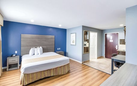 A hotel room with a large bed, a desk, a chair, and a door leading to a bathroom.