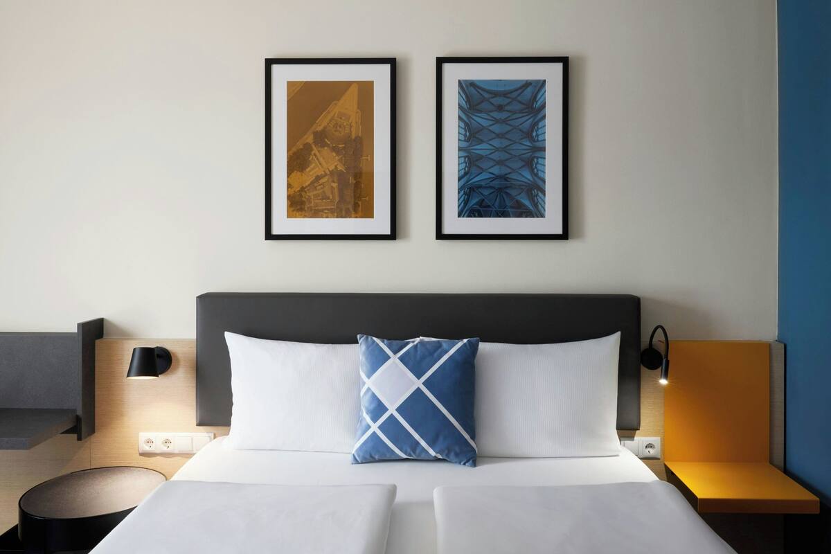 Een hotelkamer met een bed, een nachtkastje, een lamp en twee afbeeldingen in een lijst op de muur.