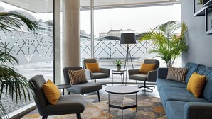 Un área de descanso moderna con un sofá, sillones y una mesa de centro, con vistas a la ciudad a través de amplios ventanales.