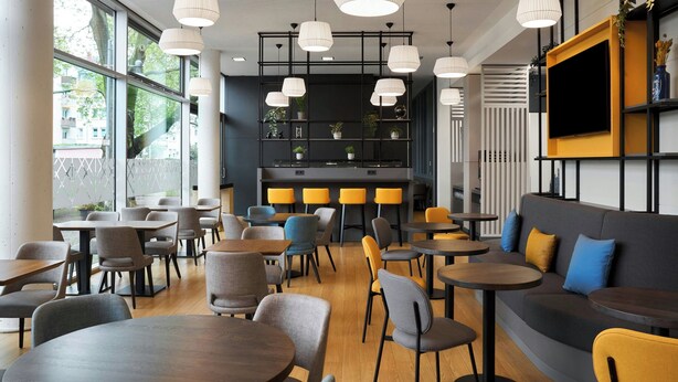 Un café moderno con mesas y sillas redondas, un sofá y un televisor montado en la pared.