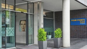 Una entrada moderna de edificio con puertas de vidrio, un pilar de hormigón grande y un letrero que dice "FOUR POINTS FLEX BY SHERATON".