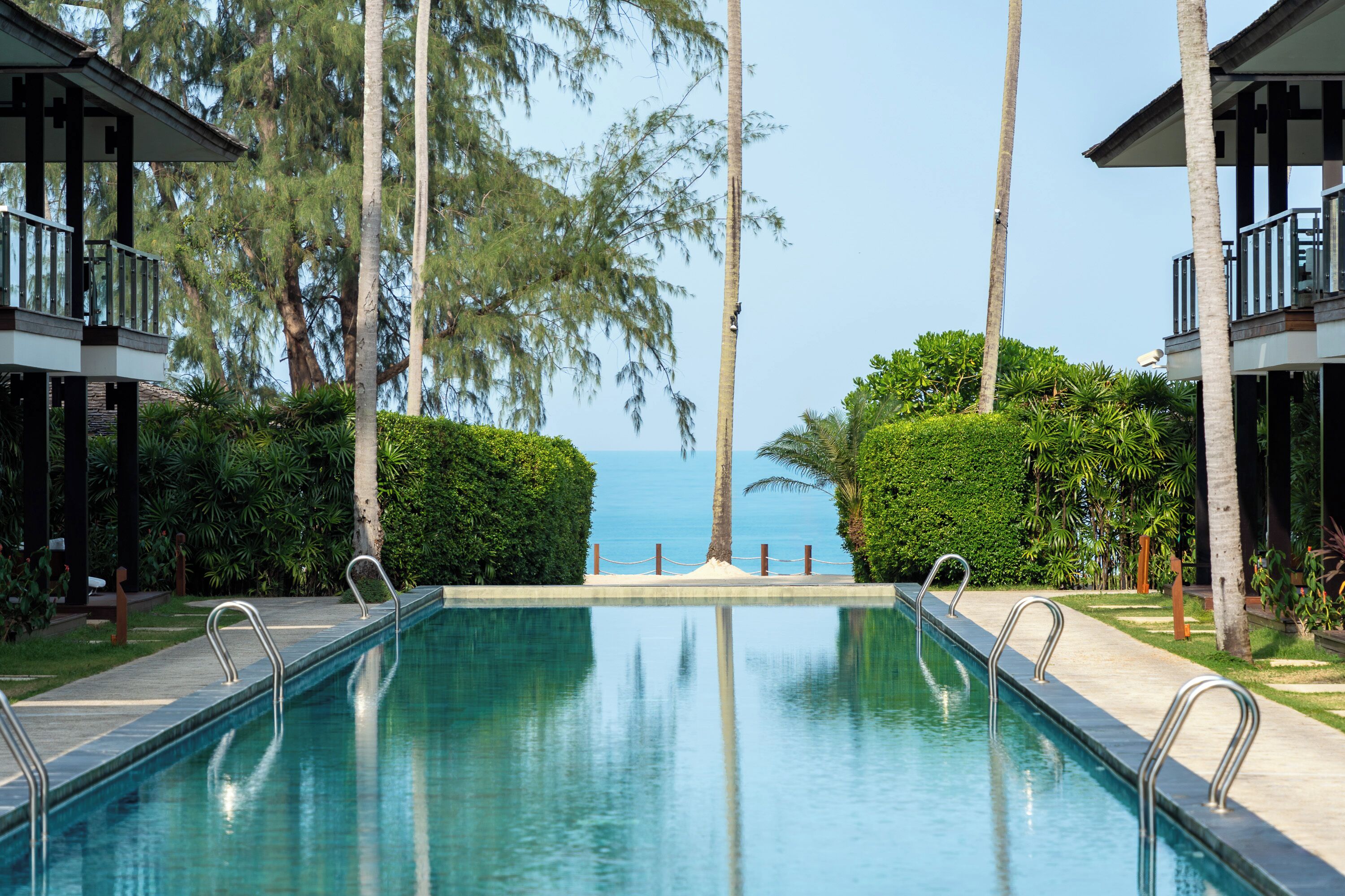 Ein Pool mit Blick auf das Meer, umgeben von Palmen und Grünpflanzen.