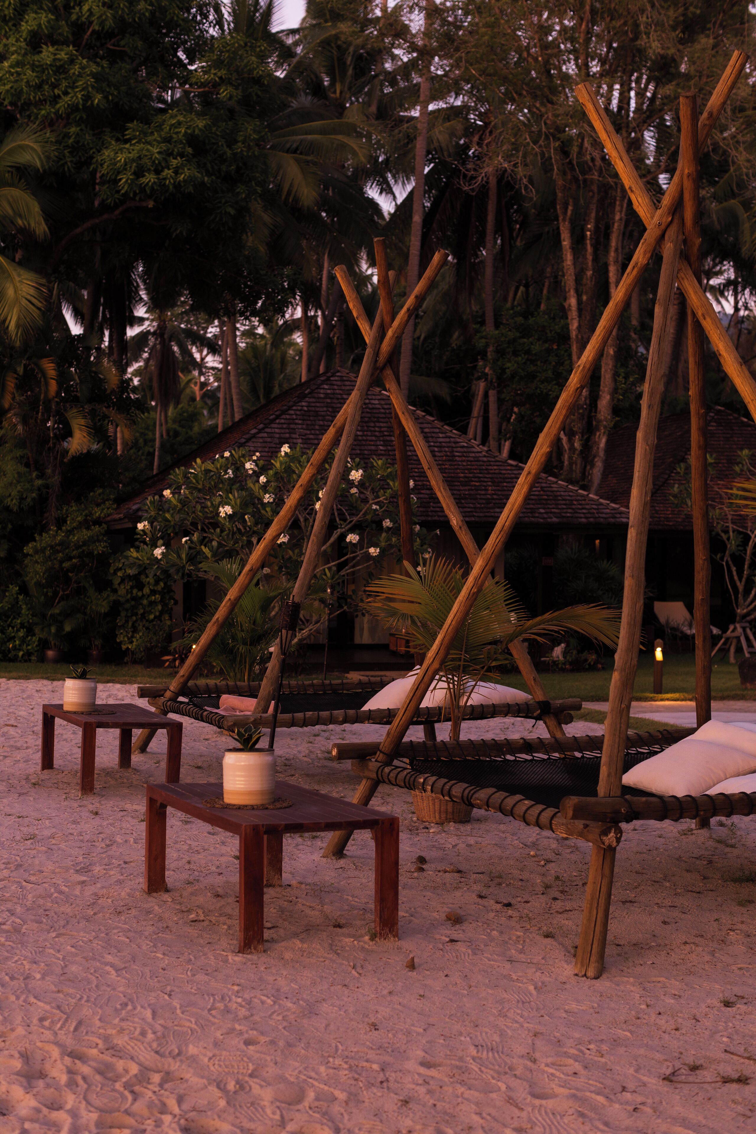 A beach setting with wooden structures, including a hammock and a small table with a candle.