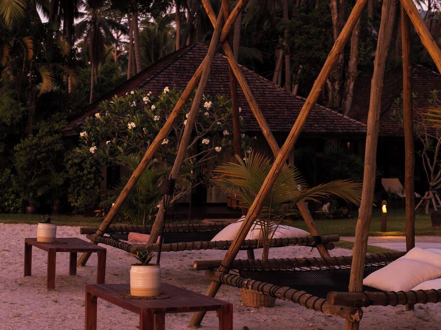 A beach setting with wooden structures, including a hammock and a small table with a candle.