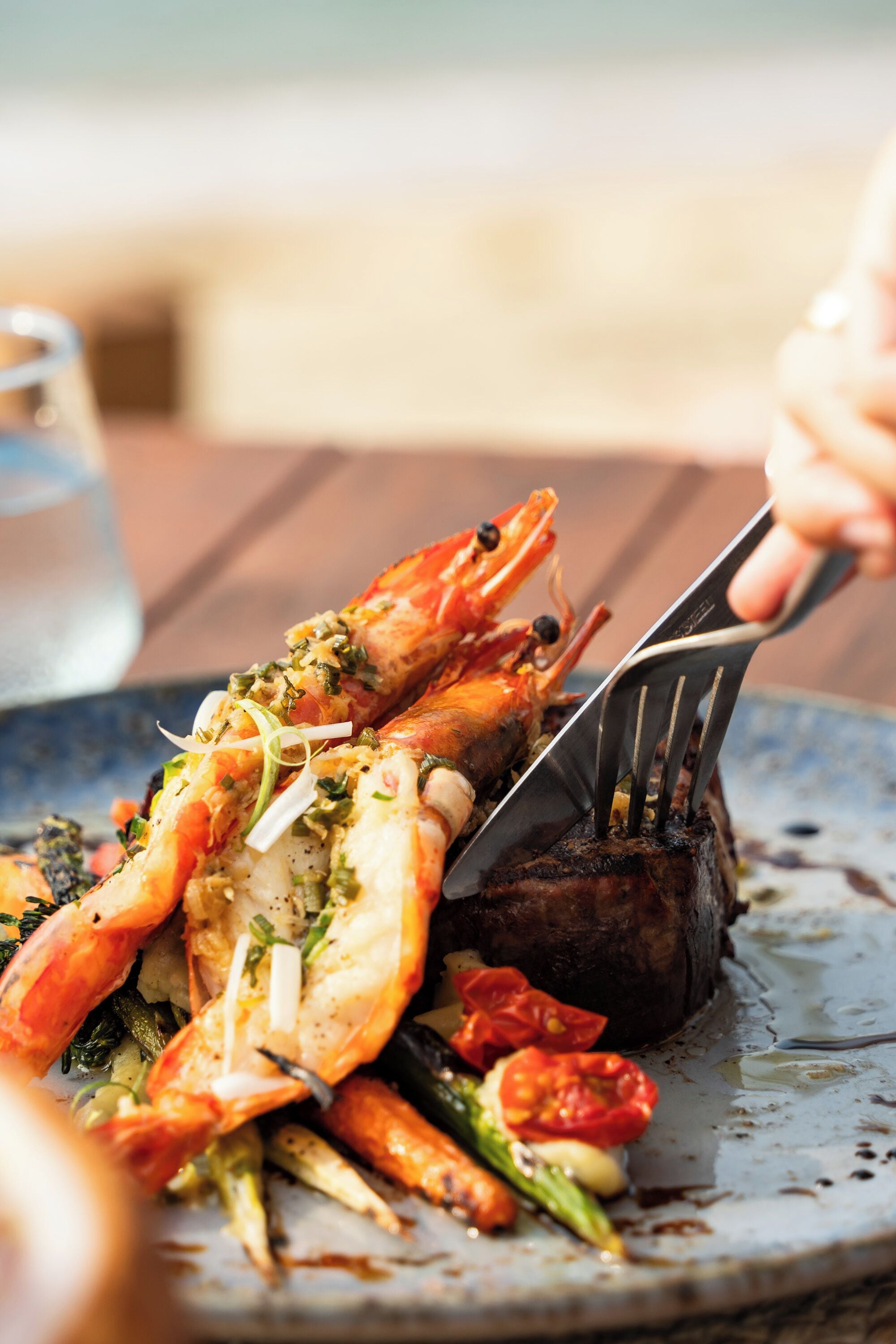 Un plato de mariscos cocidos con un tenedor y cuchillo, y un vaso de agua al fondo.