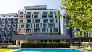 Un immeuble moderne à plusieurs étages, avec une piscine située devant.