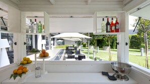 Une cuisine moderne avec des meubles blancs, un coin repas doté d’un espace extérieur et une vue sur le jardin.