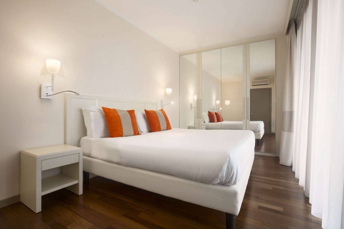 Una habitación de hotel moderna con una cama grande, una mesita de noche, un espejo y un armario.