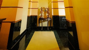 Um hall de hotel com um lustre central, um balcão de recepção e uma estátua decorativa.