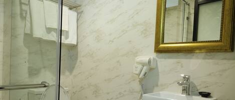 A bathroom with a glass shower enclosure, a white toilet, a black vanity with a white sink, and a gold-framed mirror.