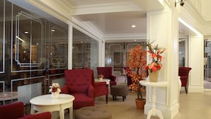 Um hall amplo com poltronas vermelhas, uma mesa branca com um vaso de flores e uma grande planta em vaso.